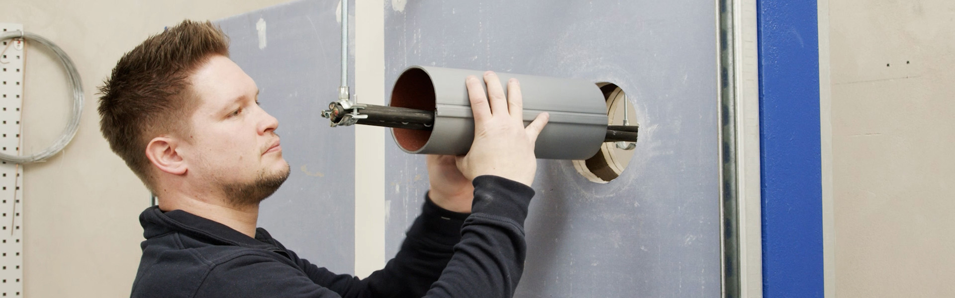 A craftsman installs a CT Cable Tube around electrical cables in a wall duct.