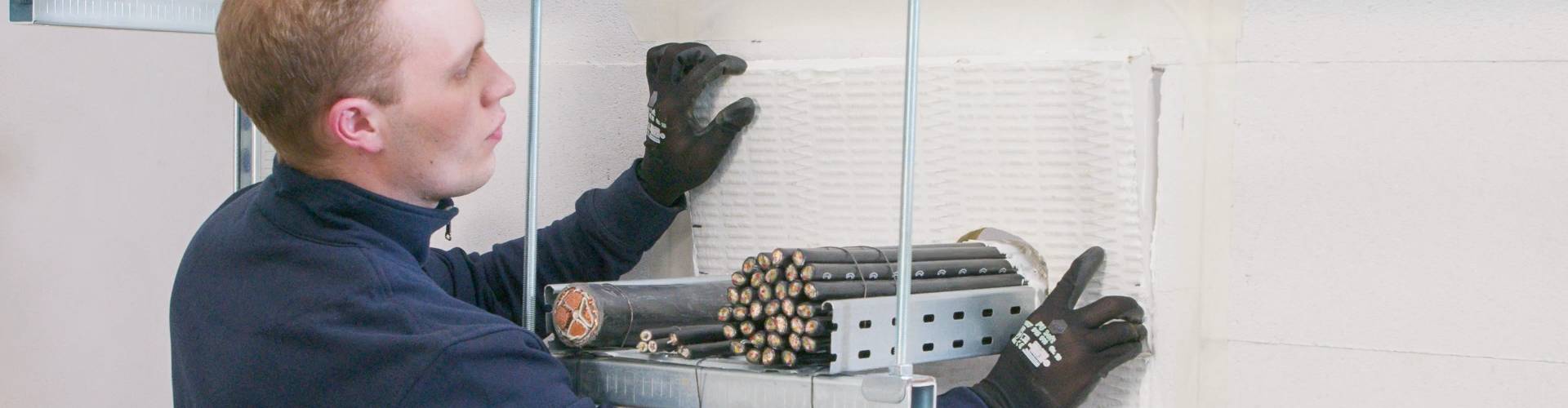 Mann in Arbeitskleidung, der Brandschutz an eine Wand anbringt.